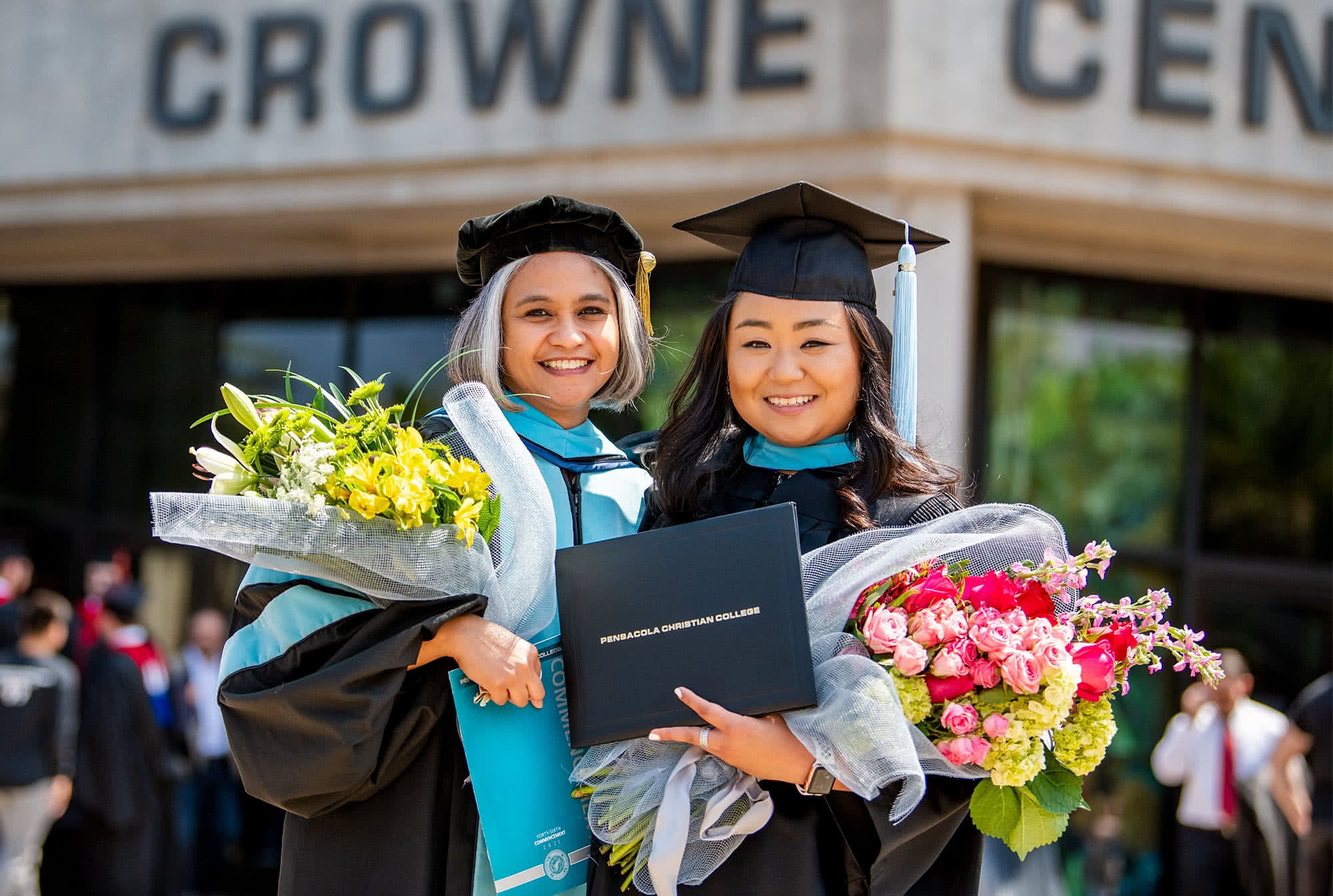 two female graduates holding flowers in front of Crowne Centre