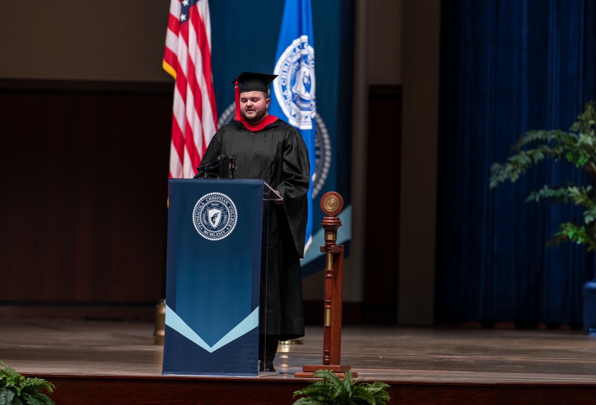 Male PCC graduate standing at podium during virtual graduation. 