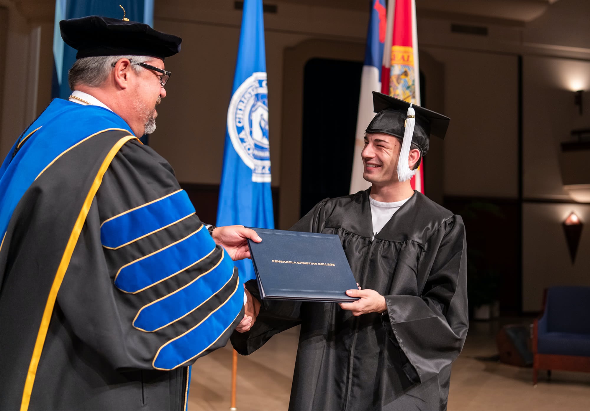 Dr. Shoemaker shaking hands with a graduate and handing him his diploma. 