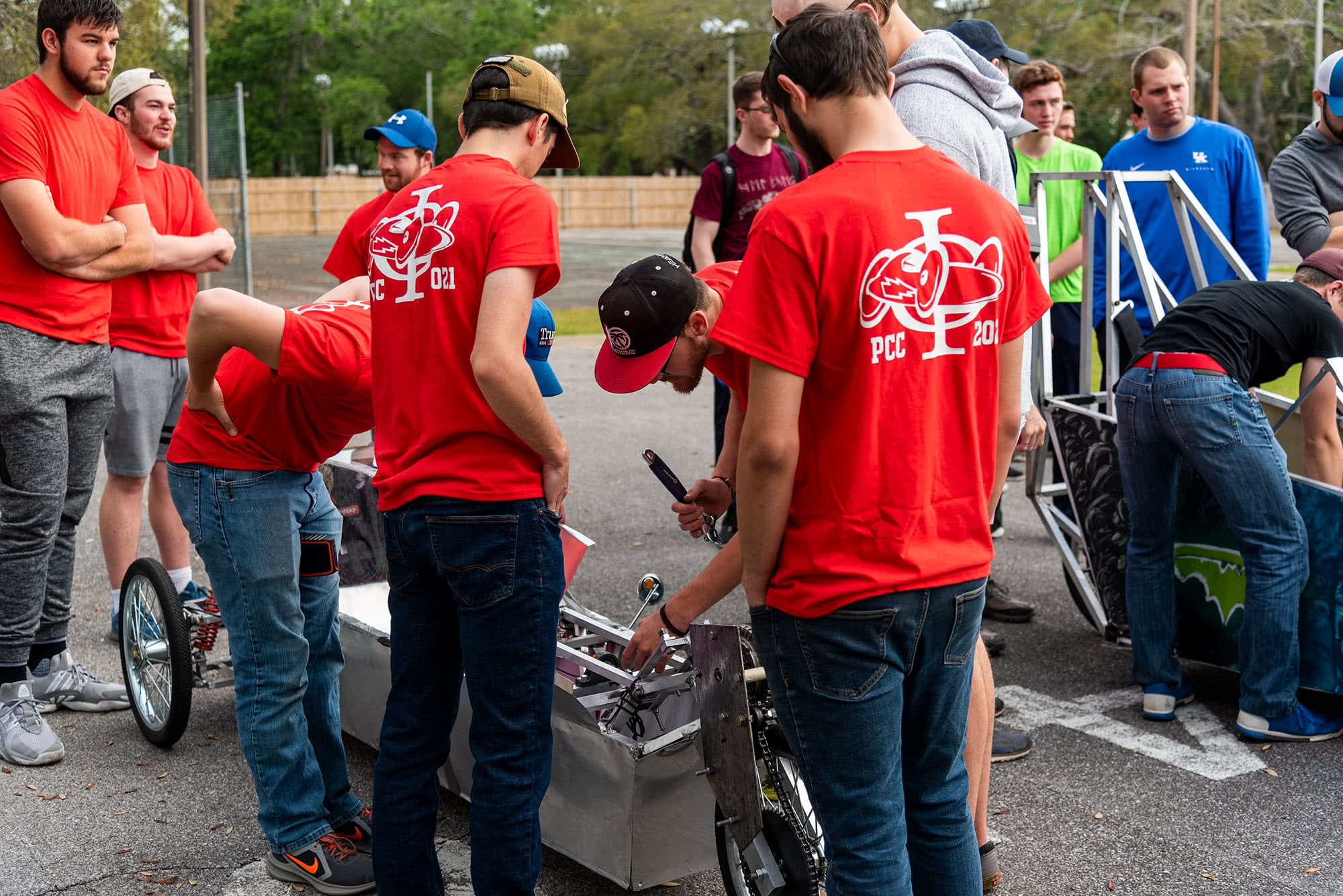 Male students in red shirts standing over and inspecting an electric vehicle. 