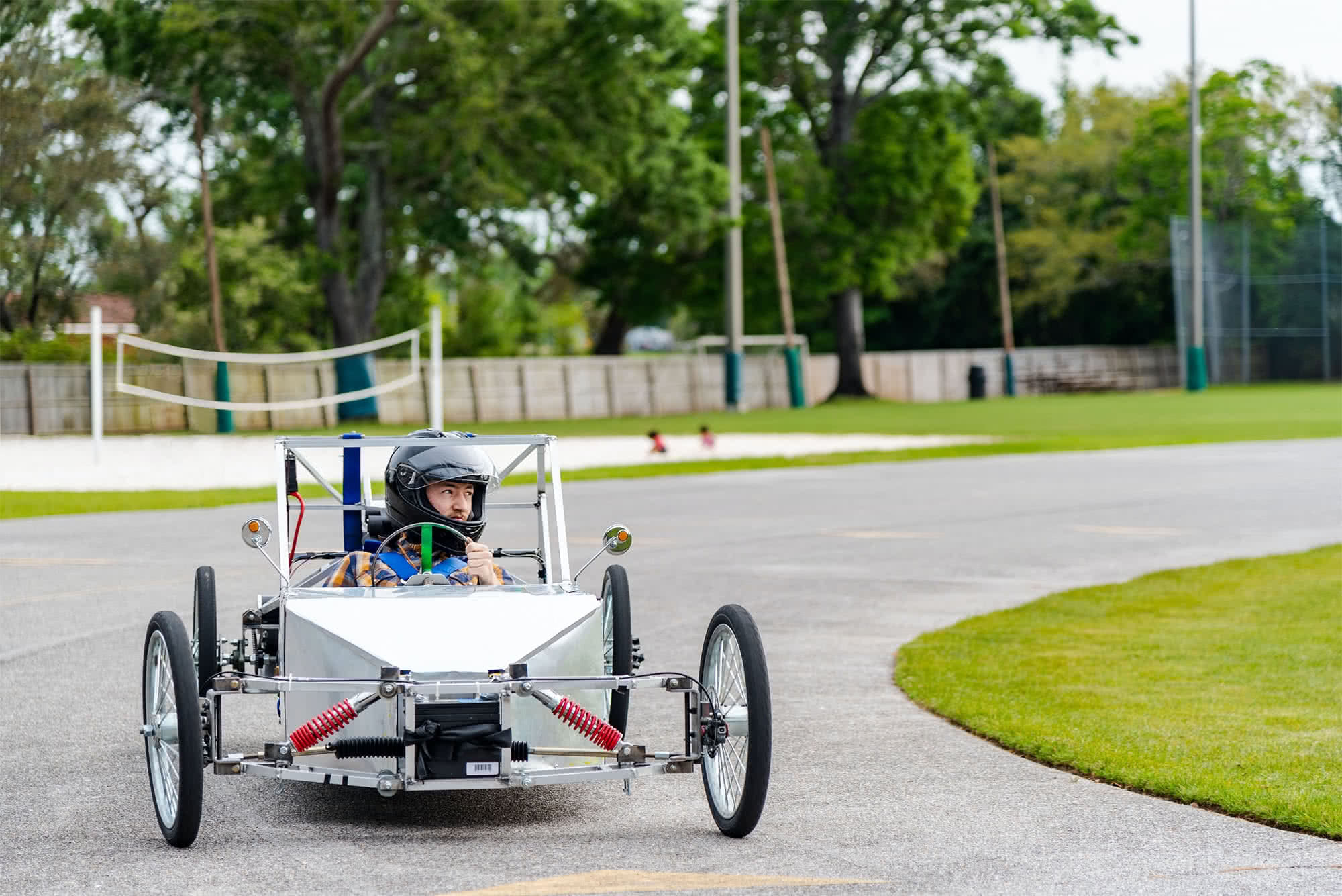 Student making a turn in a silver electric vehicle while wearing a helmet. 