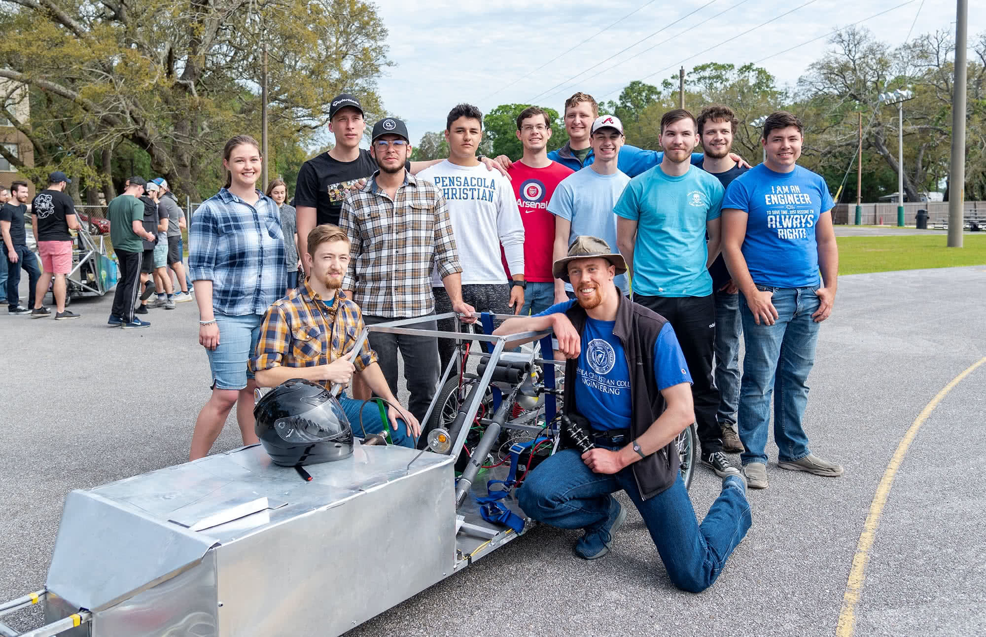 Students gathered around a silver electric vehicle and posing for a picture. 