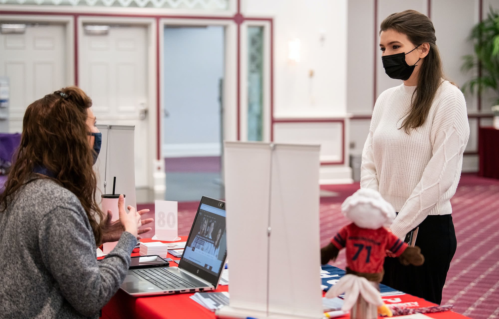 Female student speaking to a woman sitting behind a booth at the Health Professions Career Fair. 