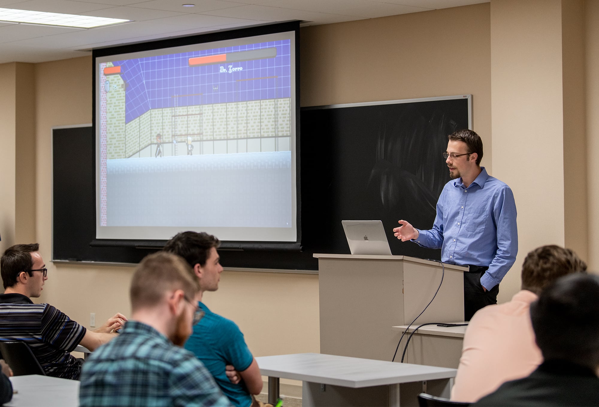 Man standing in front of a class of students and presents a video game. 