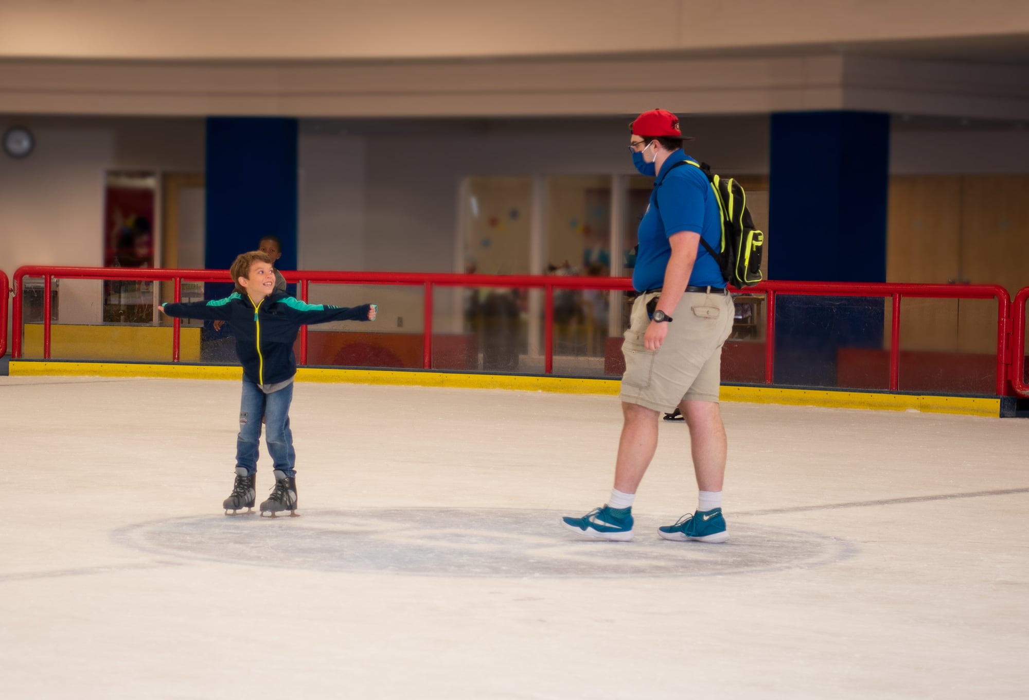 Sports Center Day Camp counselor standing with a camper on the ice skating rink. 