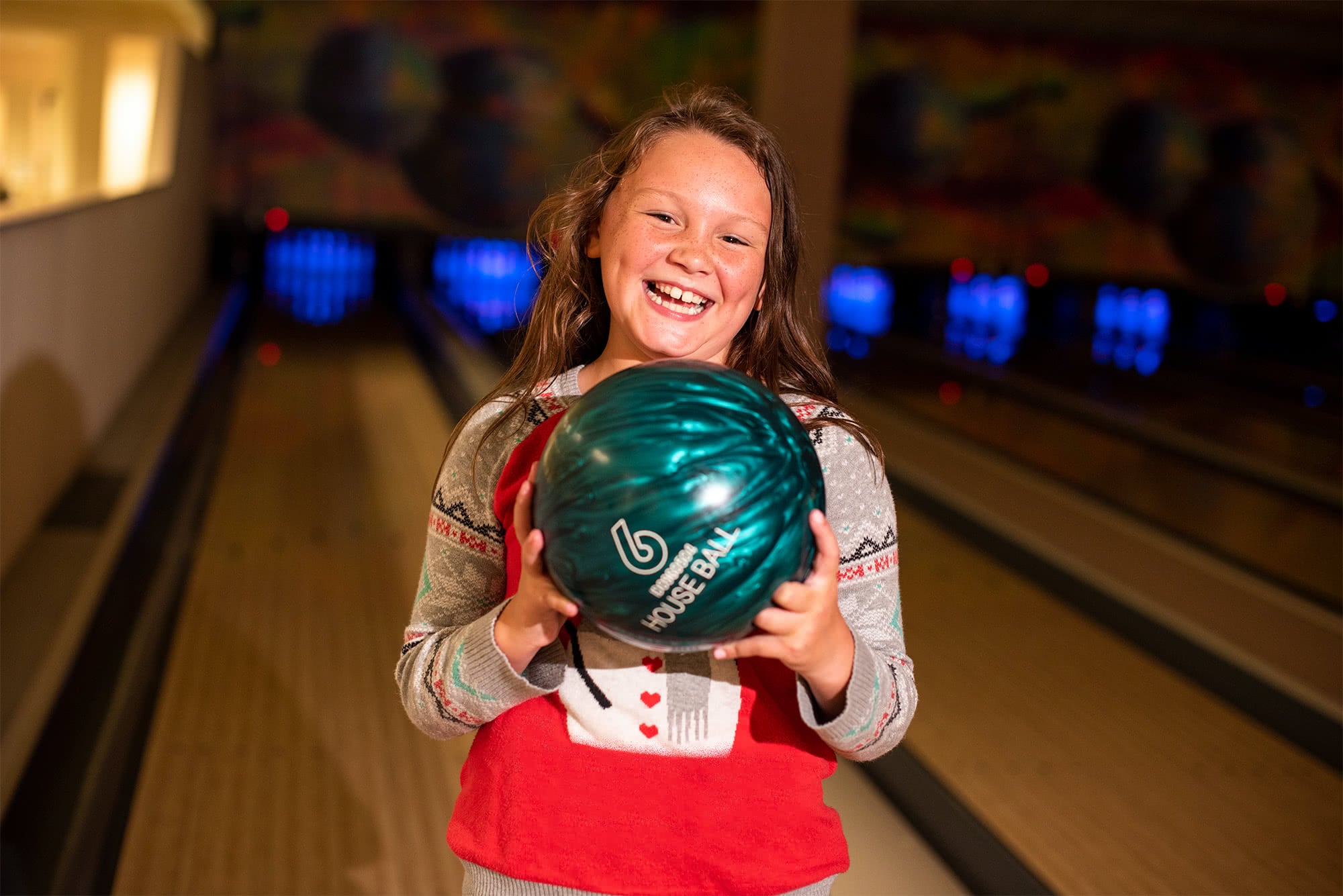 Sports Center Day Camp camper smiling and holding a bowling ball. 