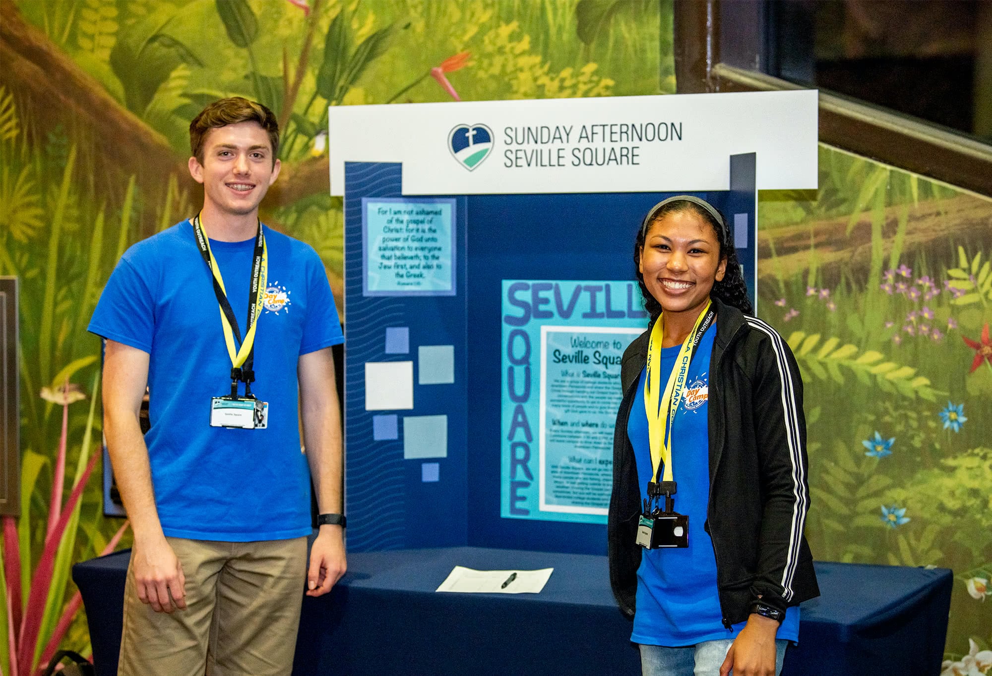 Two student Summer Day Camp workers standing in front of a display table. 