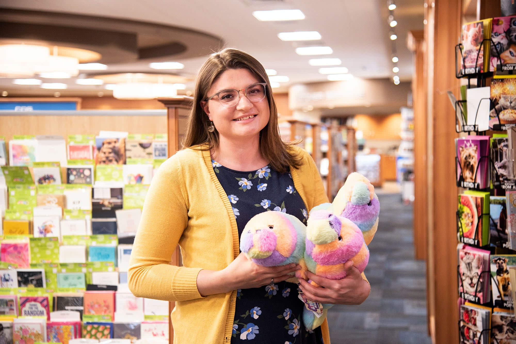 Female student campus store worker holding stuffed animals. 