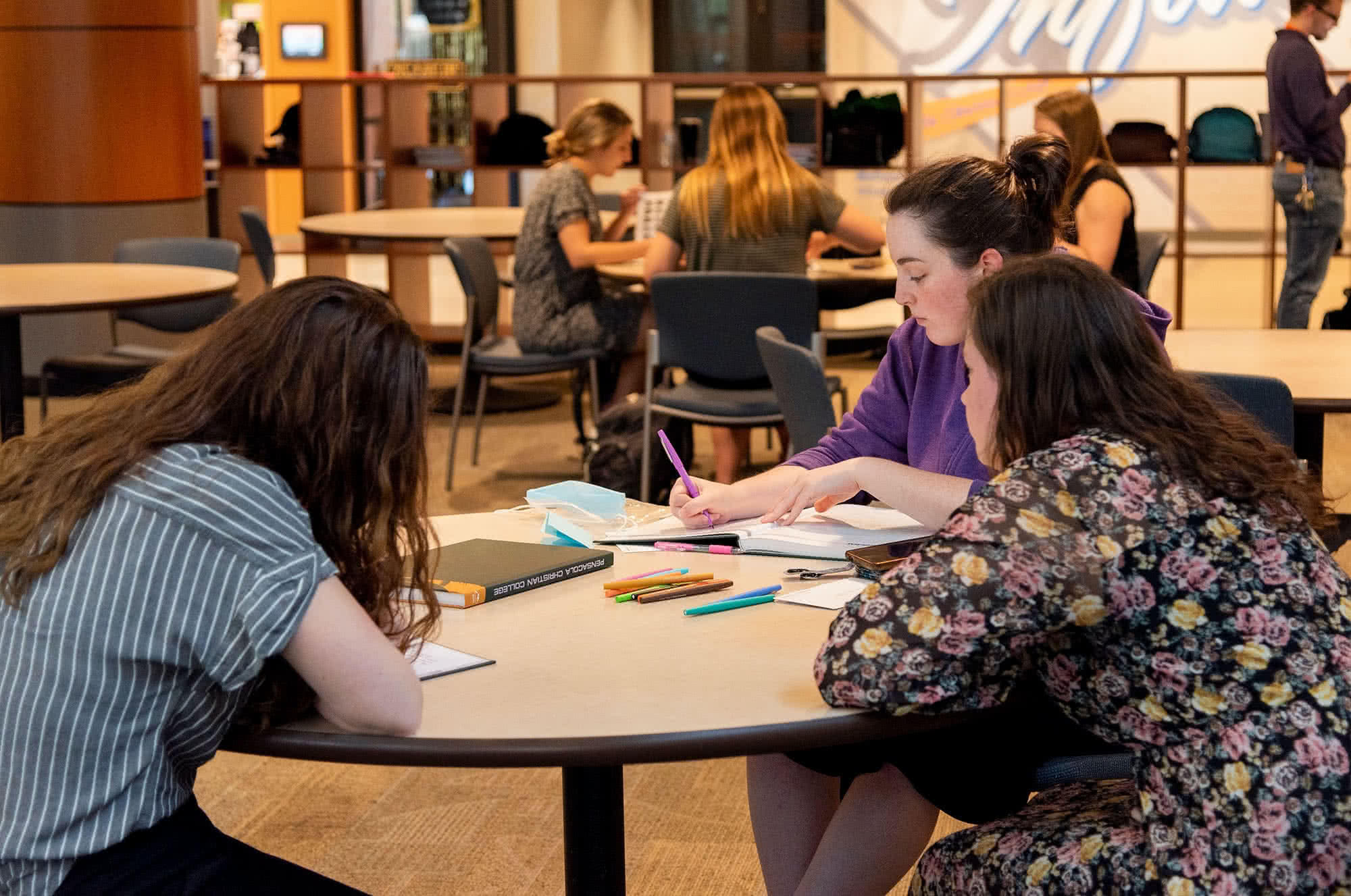 Three female students sitting in the PCC Commons and writing in Summit yearbooks. 