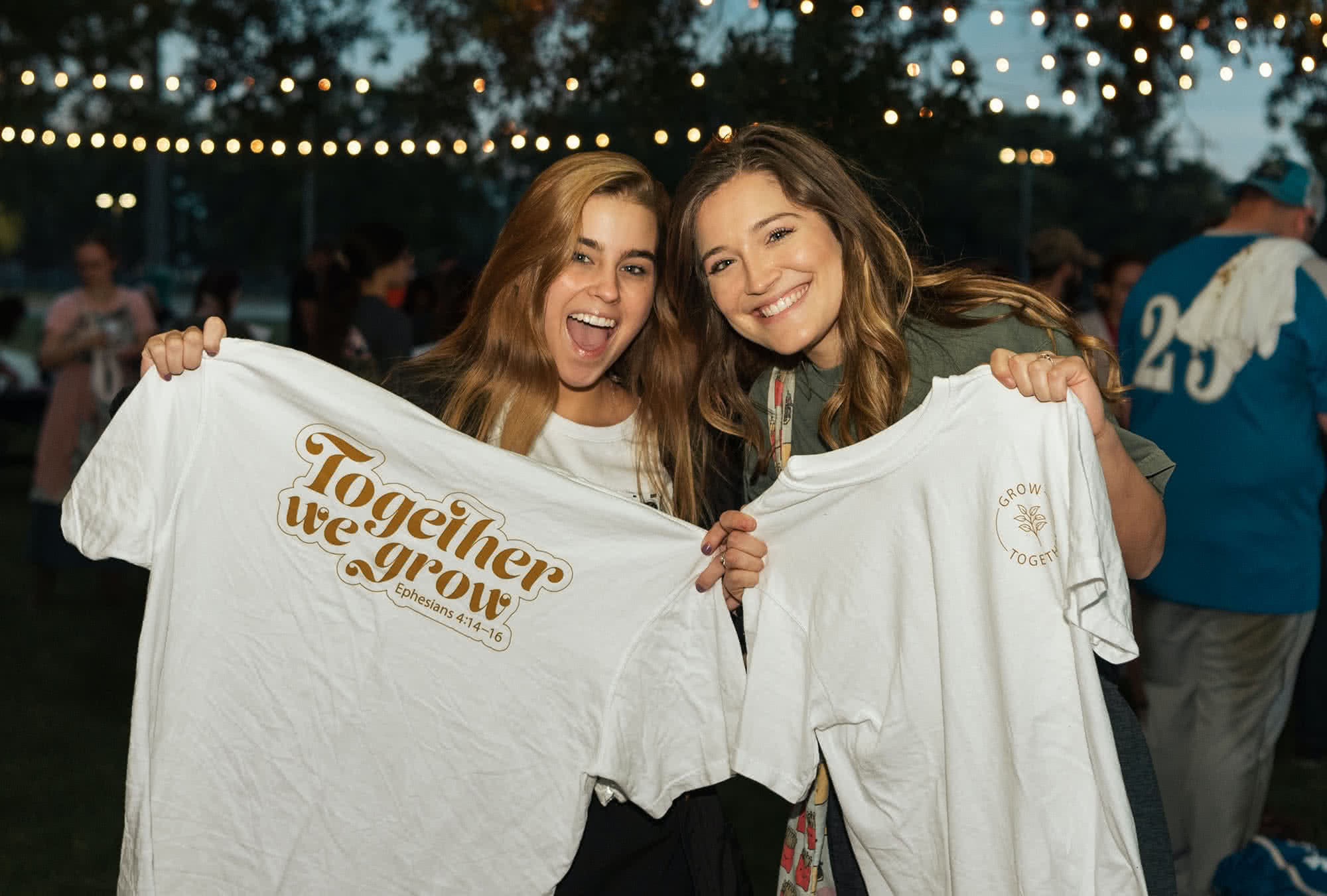 Two female students smiling and holding t-shirts.