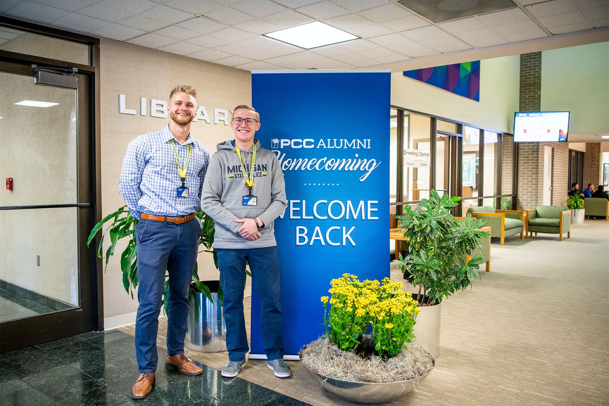 Two male PCC students standing in front a the PCC Alumni Homecoming sign. 