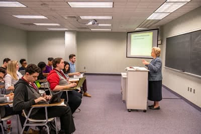 Dr. Monk standing at a podium and teaching a class of students. 