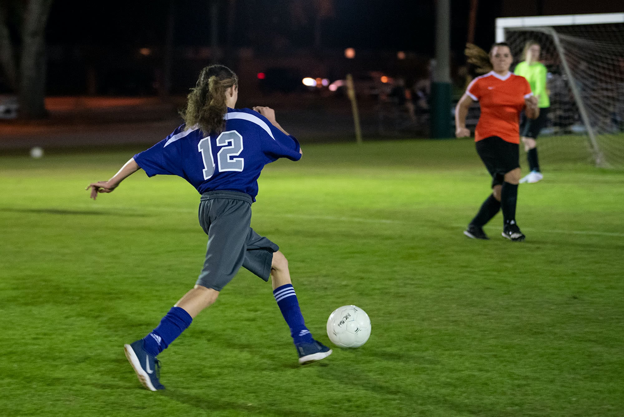 Women's collegian soccer player aiming to kick a soccer ball into the goal. 