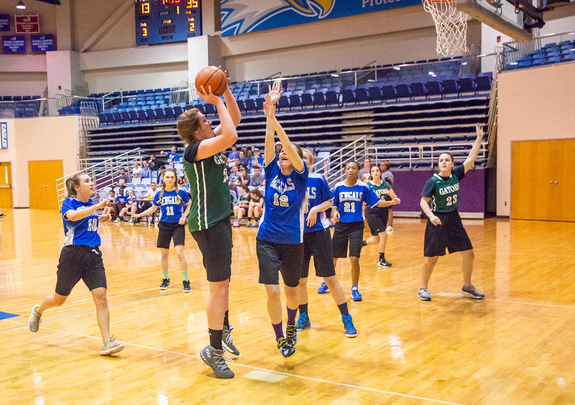 Women's collegian basketball player aiming the basketball while another player attempts to block her. 