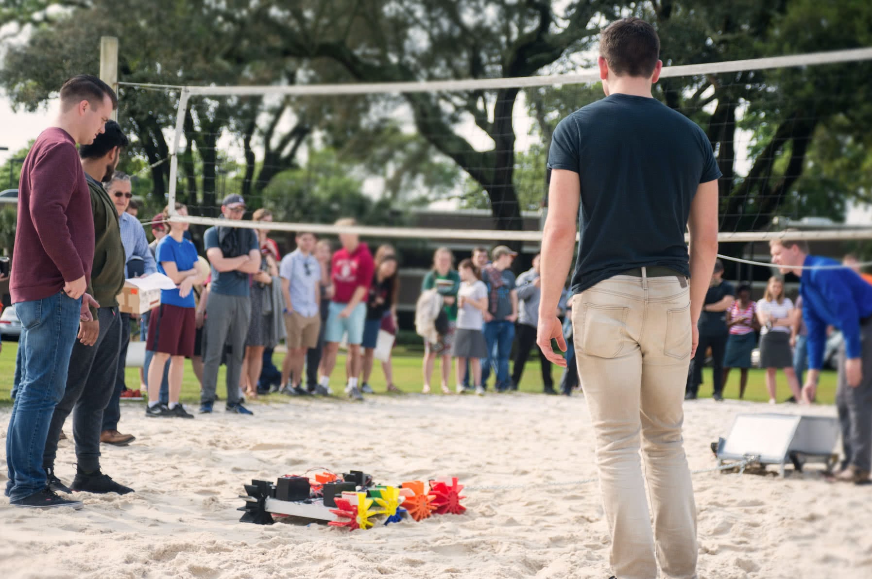 Students gathered around watching two robots play tug o' war on the sand volleyball court for the Engineering Design Contest.