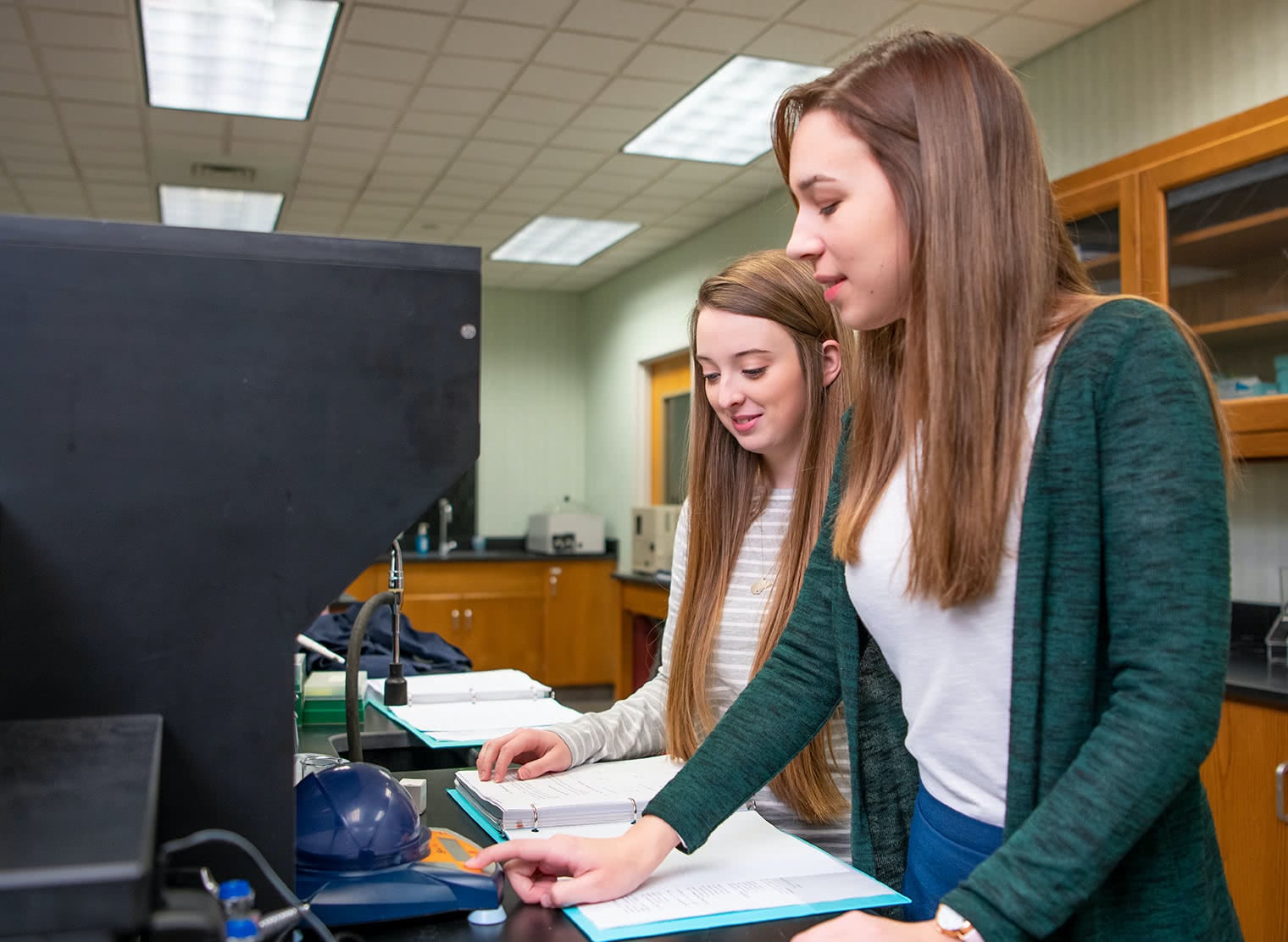 Two female students standing at a lab table and pushing a button on a machine at the start of the new semester.