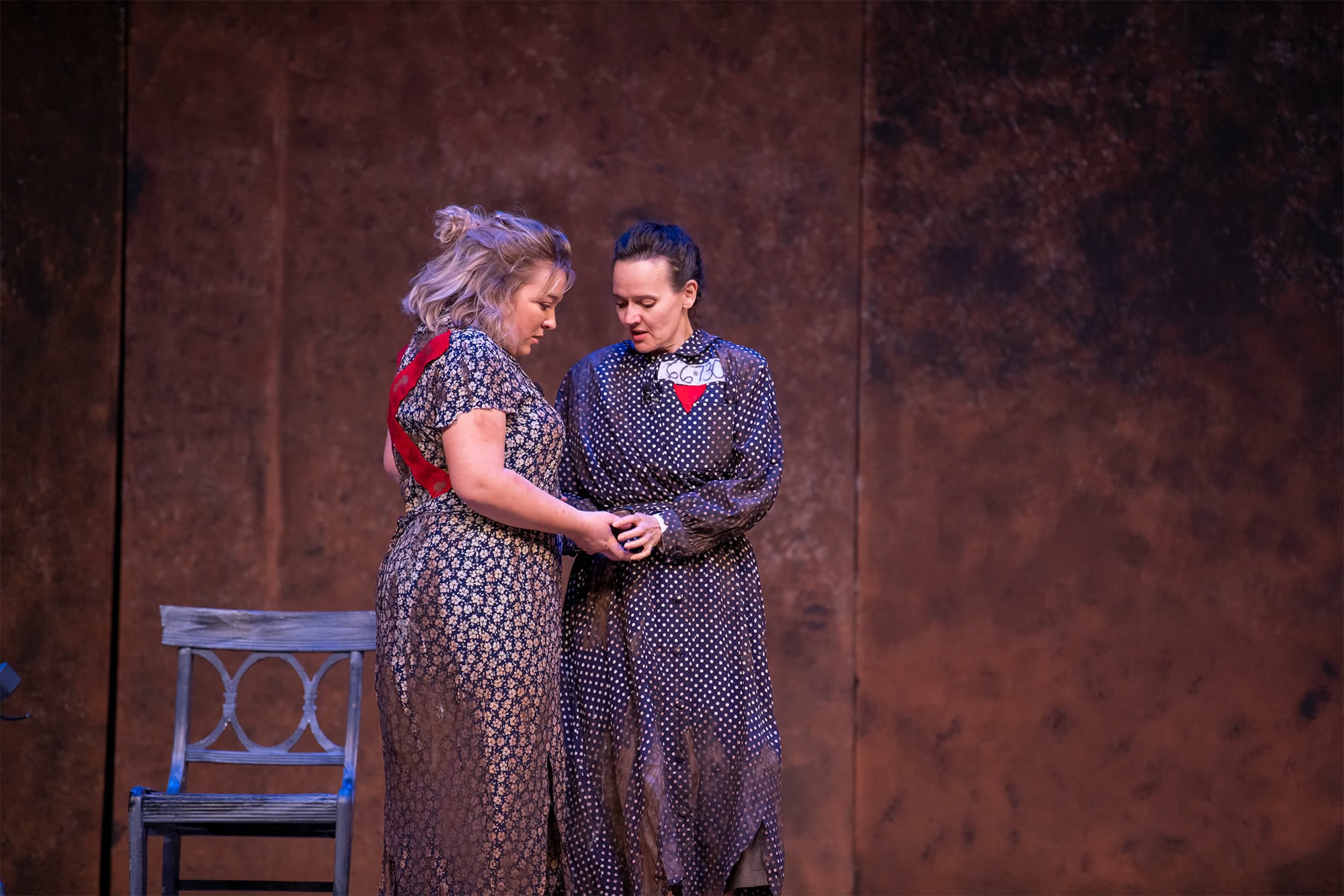 Two women in ragged dresses holding hands and talking to one another. 