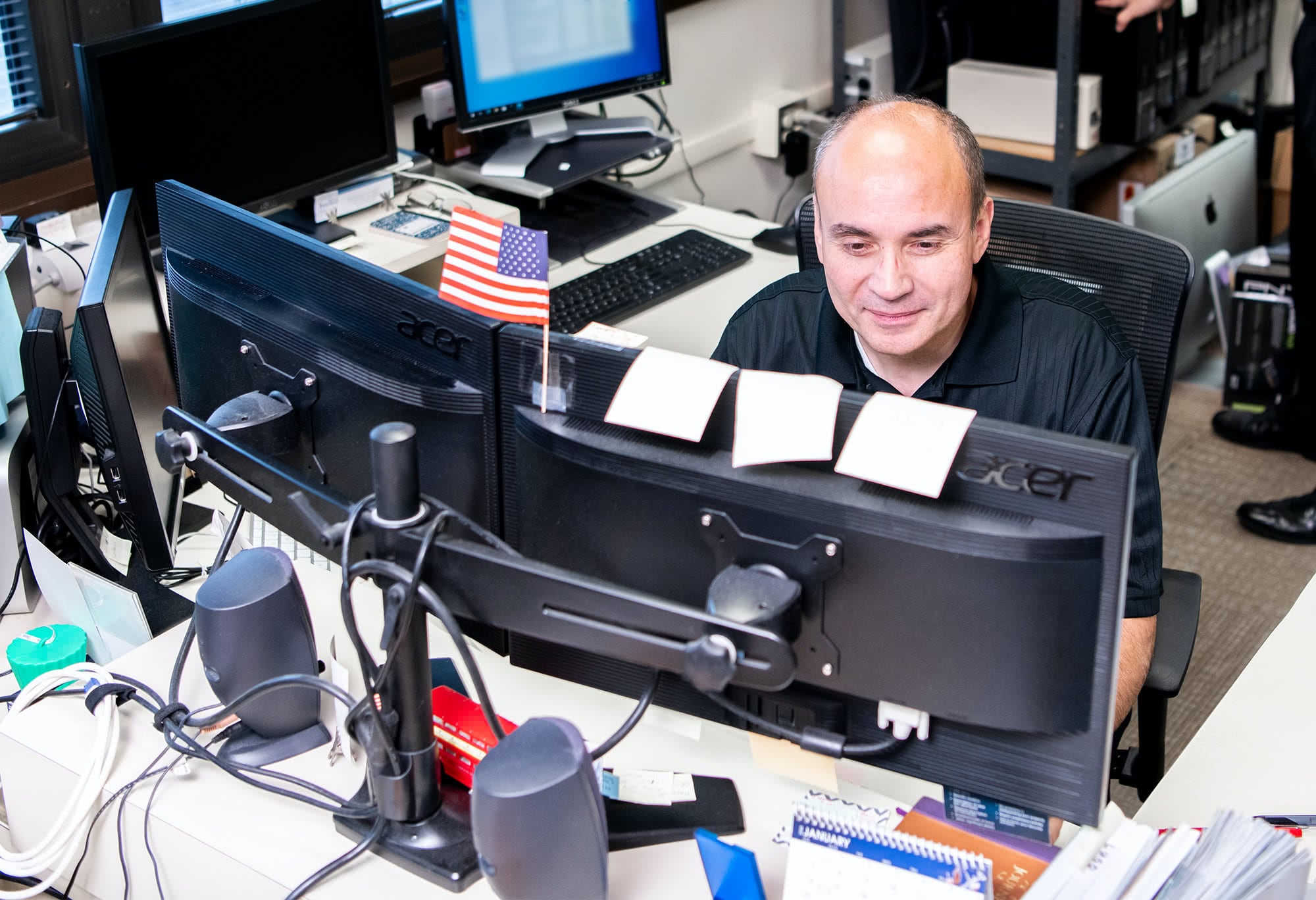 IT staff member works behind two computer monitors at his desk.