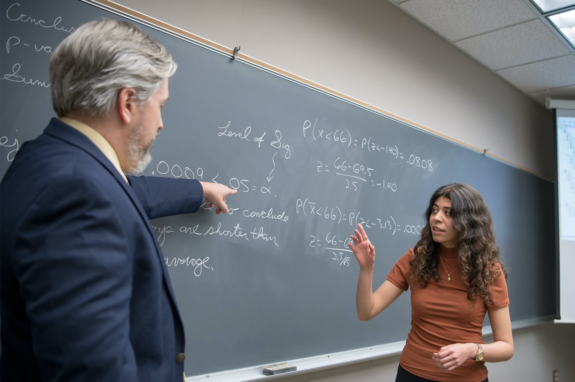 Professor pointing to the chalkboard and showing an equation to a graduate student. 