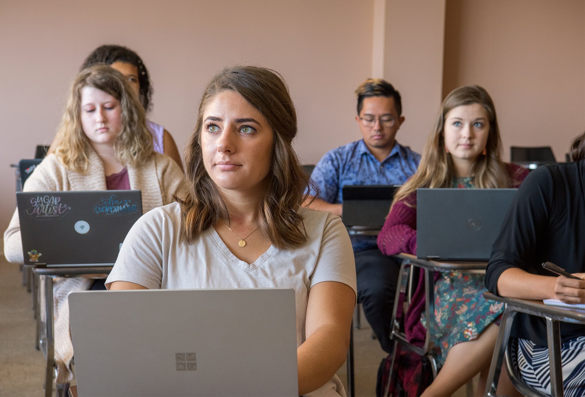 Graduate students sitting with their laptops at desks in a classroom. 
