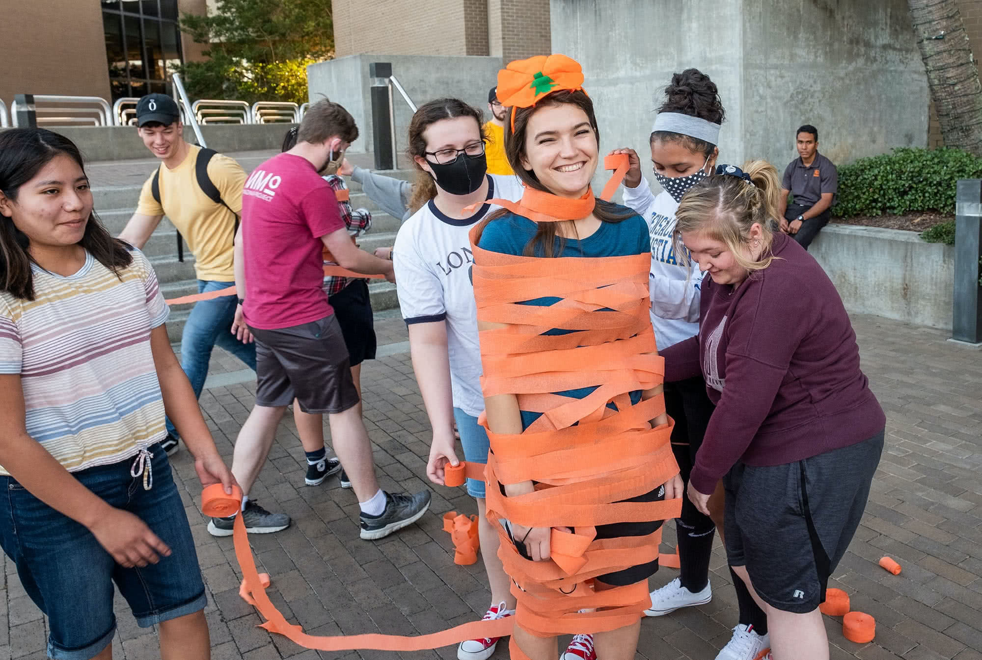 Female students wrapping another female student in orange streamers.