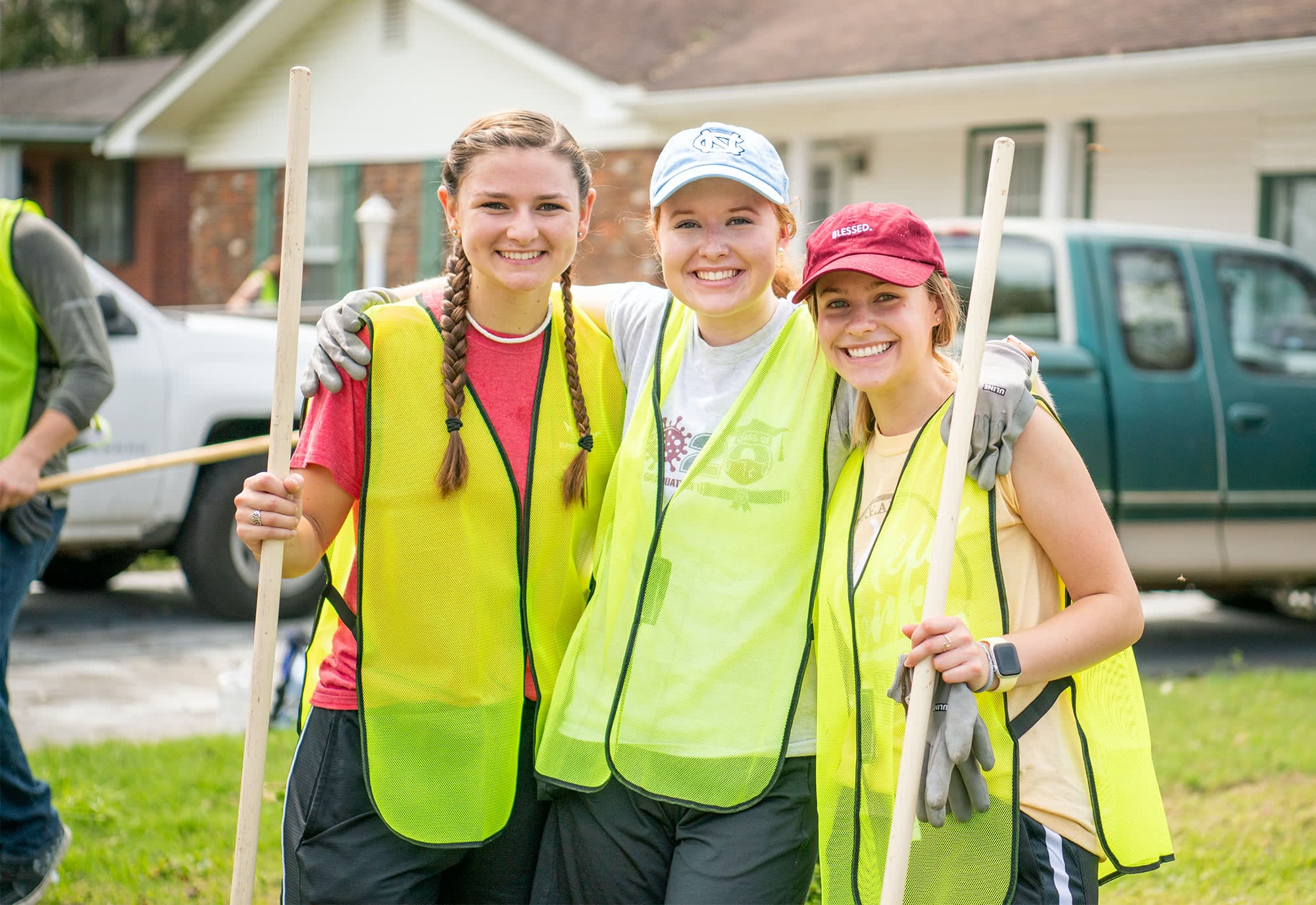 Three female students pose for a picture during clean up of a nearby neighborhood
