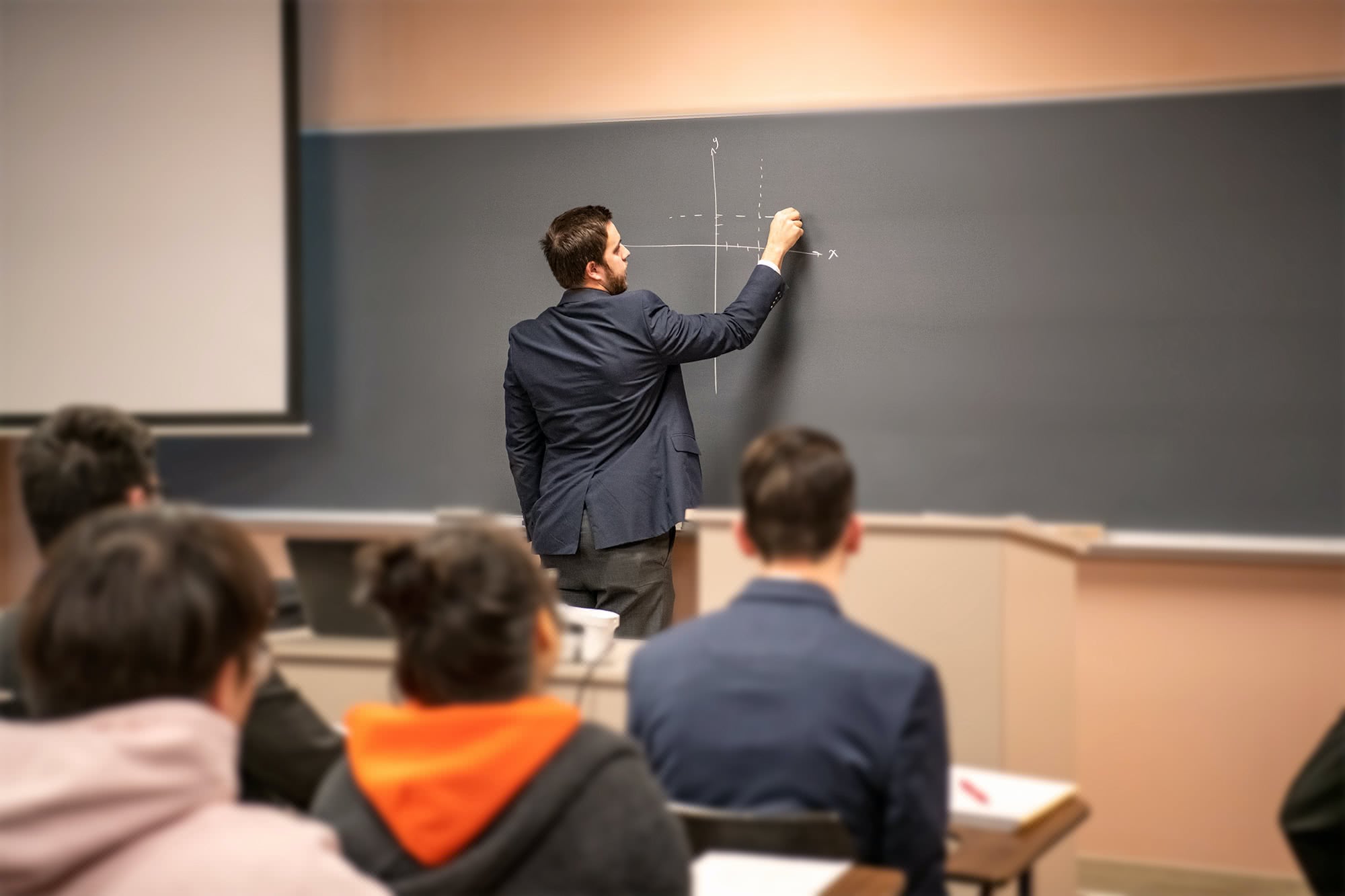 Male  interterm teacher plotting on a graph on a chalkboard.