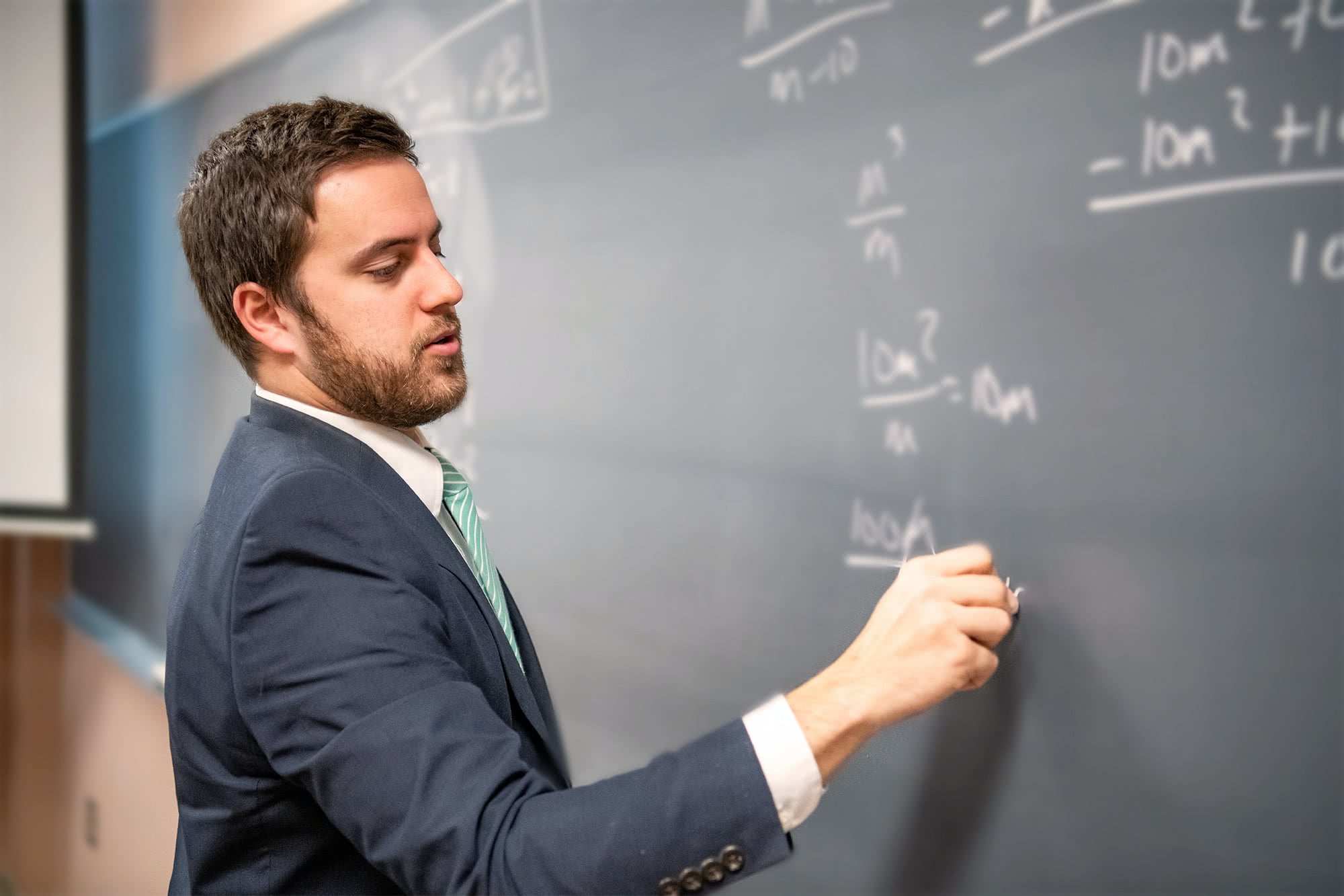 Male interterm teacher writing with chalk on a chalkboard.