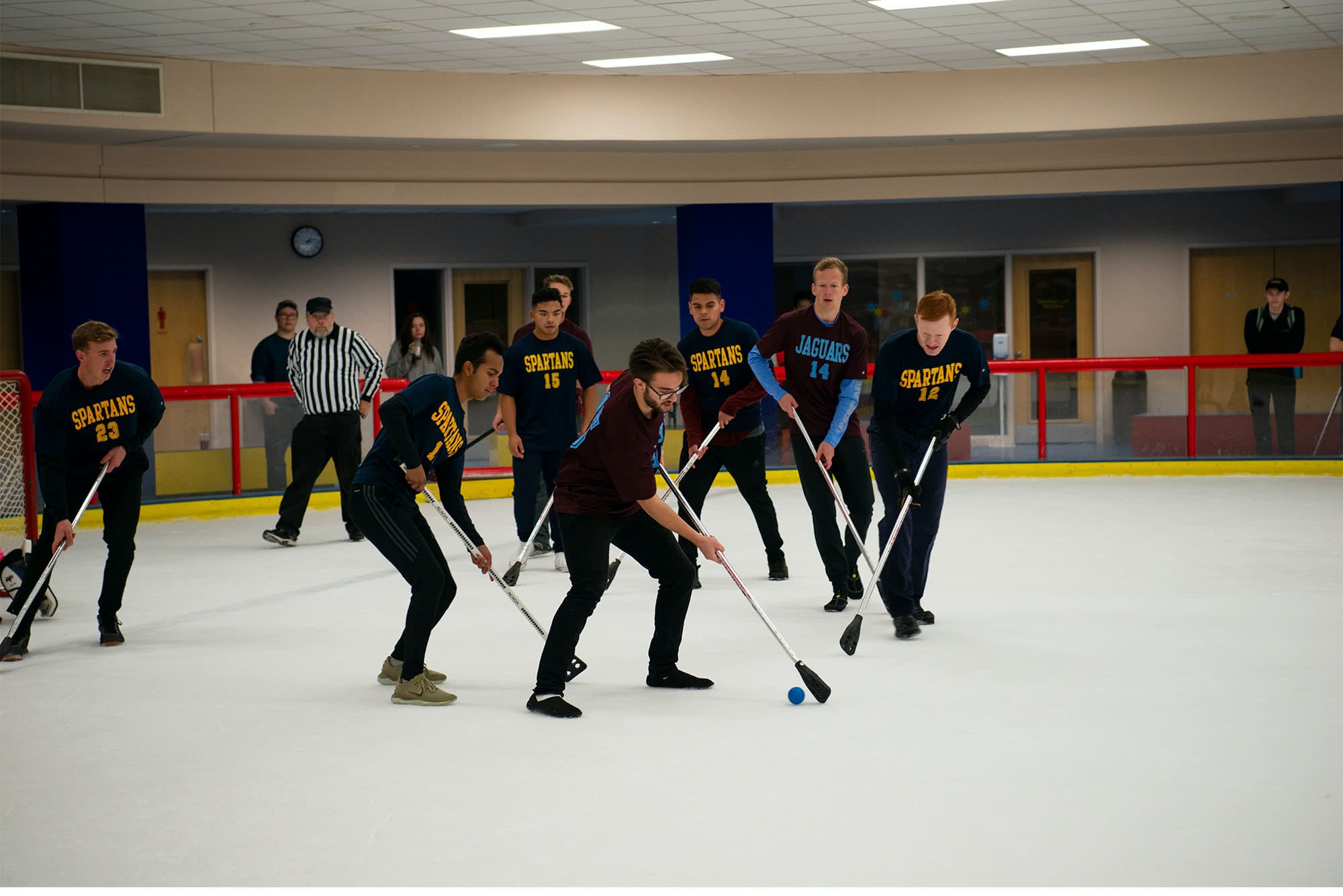 Men's collegian broom hockey players trying to steal the puck.  