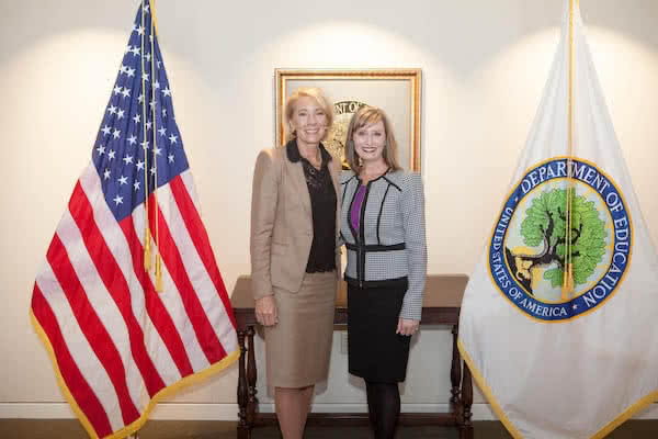 Melissa Newport and Secretary Betsy DeVos standing together between two flags. 