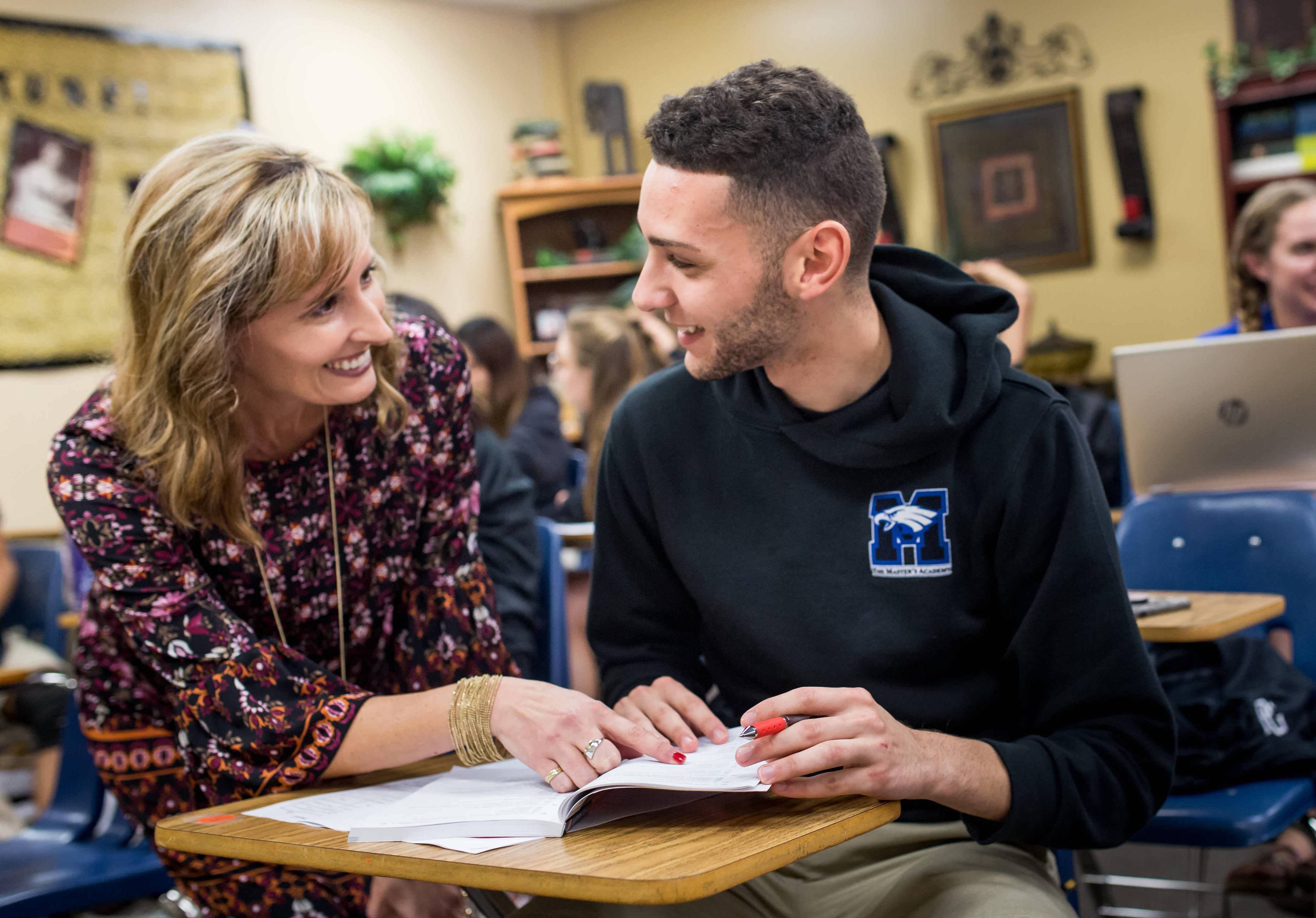 Melissa Newport helping a male student at their desk. 