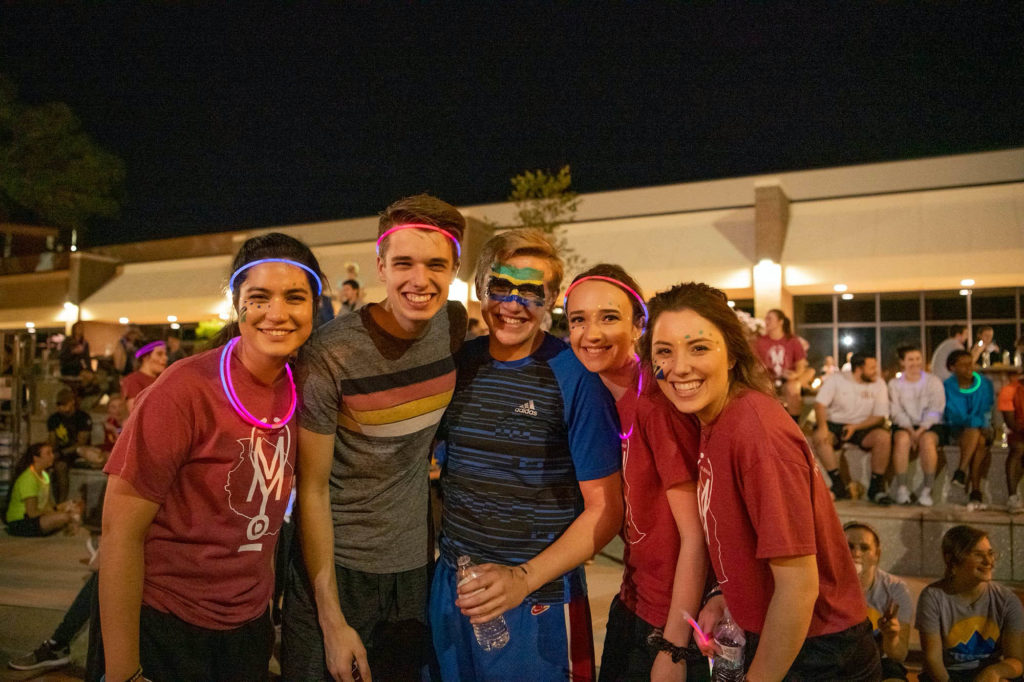 A group of friends wearing face paint and glow sticks pose together after the race