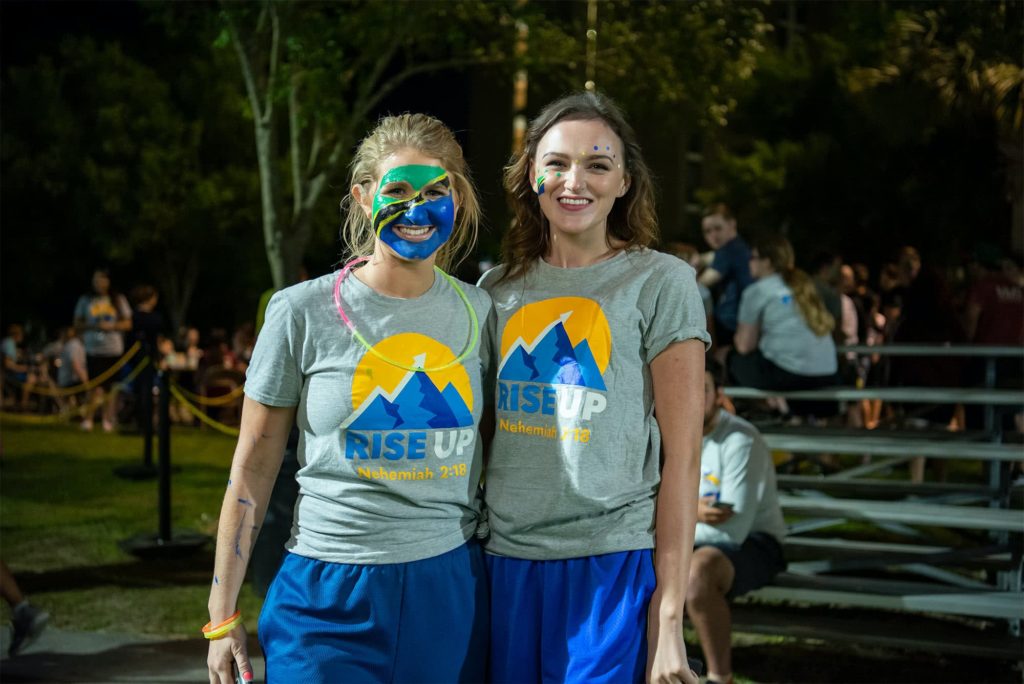 Two girls pose together before the run, they are both wearing face paint, matching t-shirt and shorts