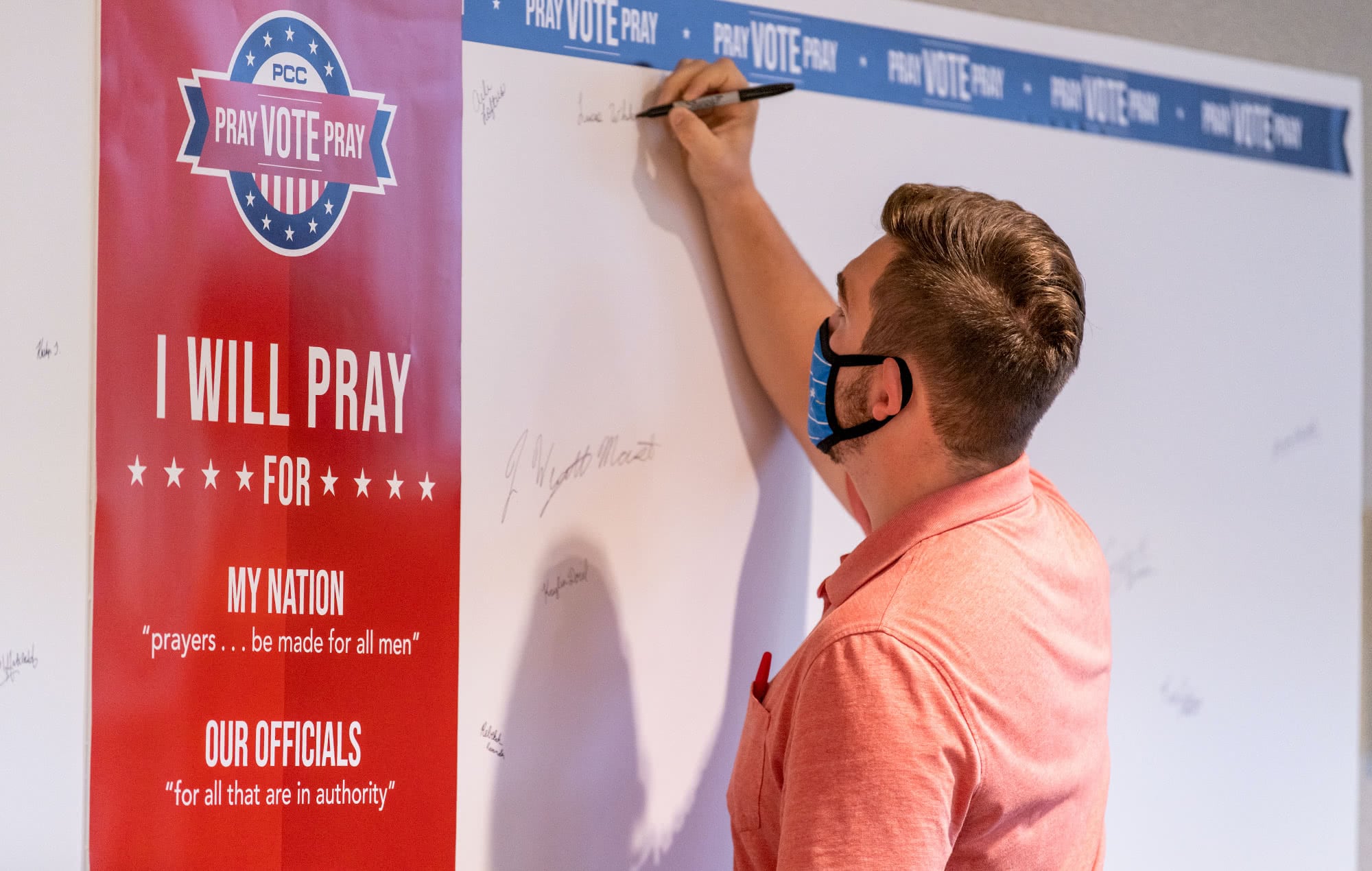 Male PCC student writing on the Student Body "Pray, Vote, Pray" board. 