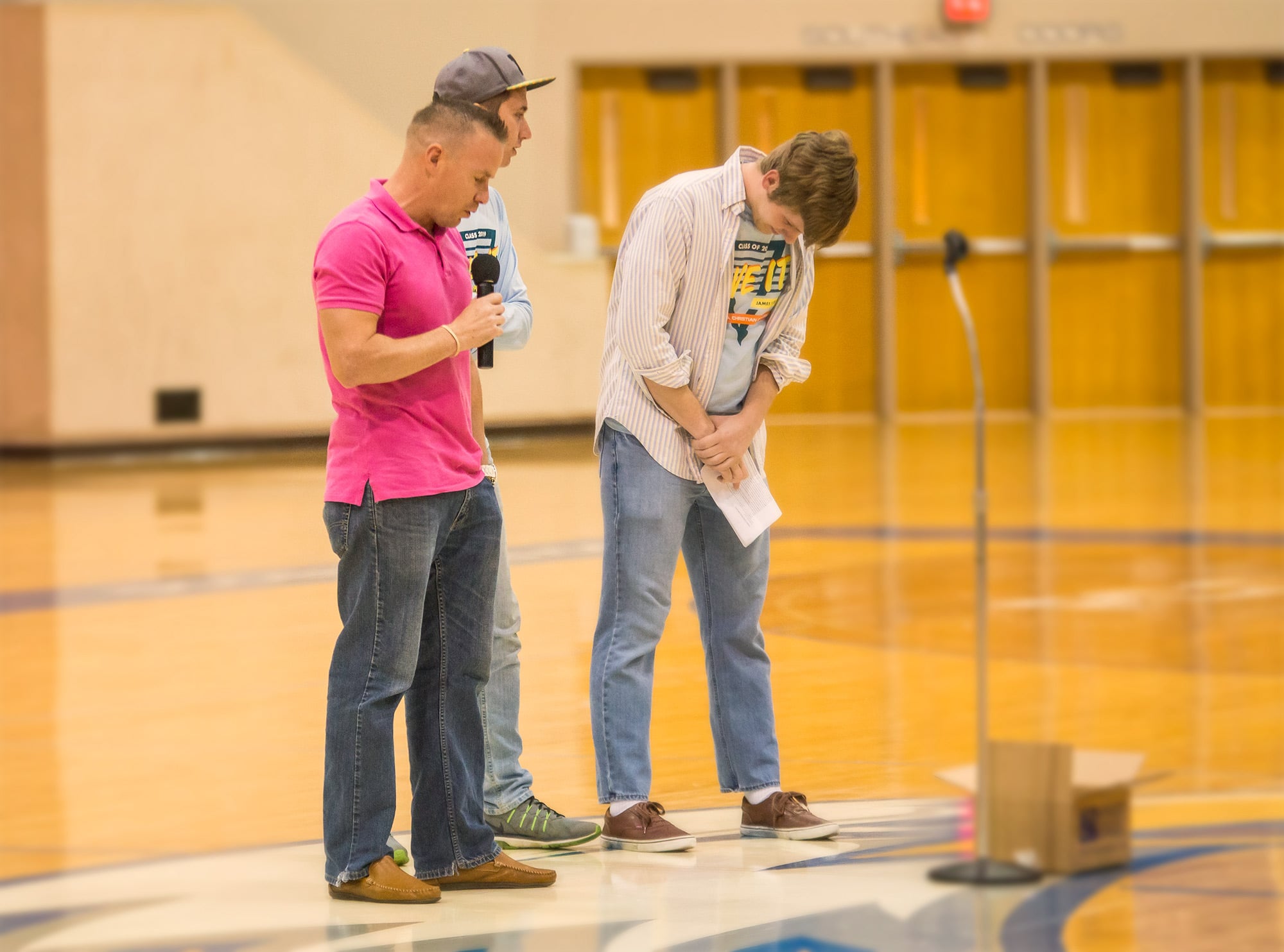 Three male students standing on the gym floor for prayer at their senior class party..