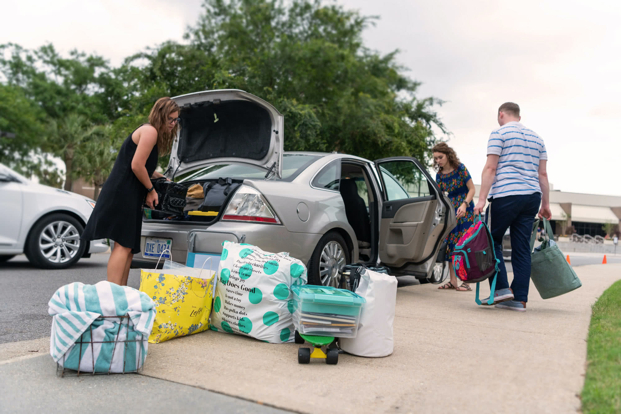 Two girls and a guy pack a car to leave for the summer