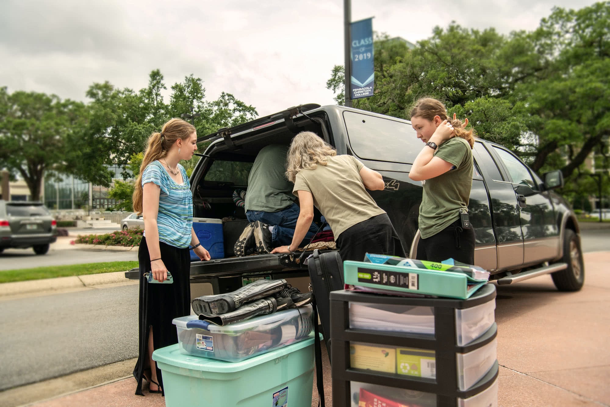 A mom helps her two daughters pack a car full of stuff