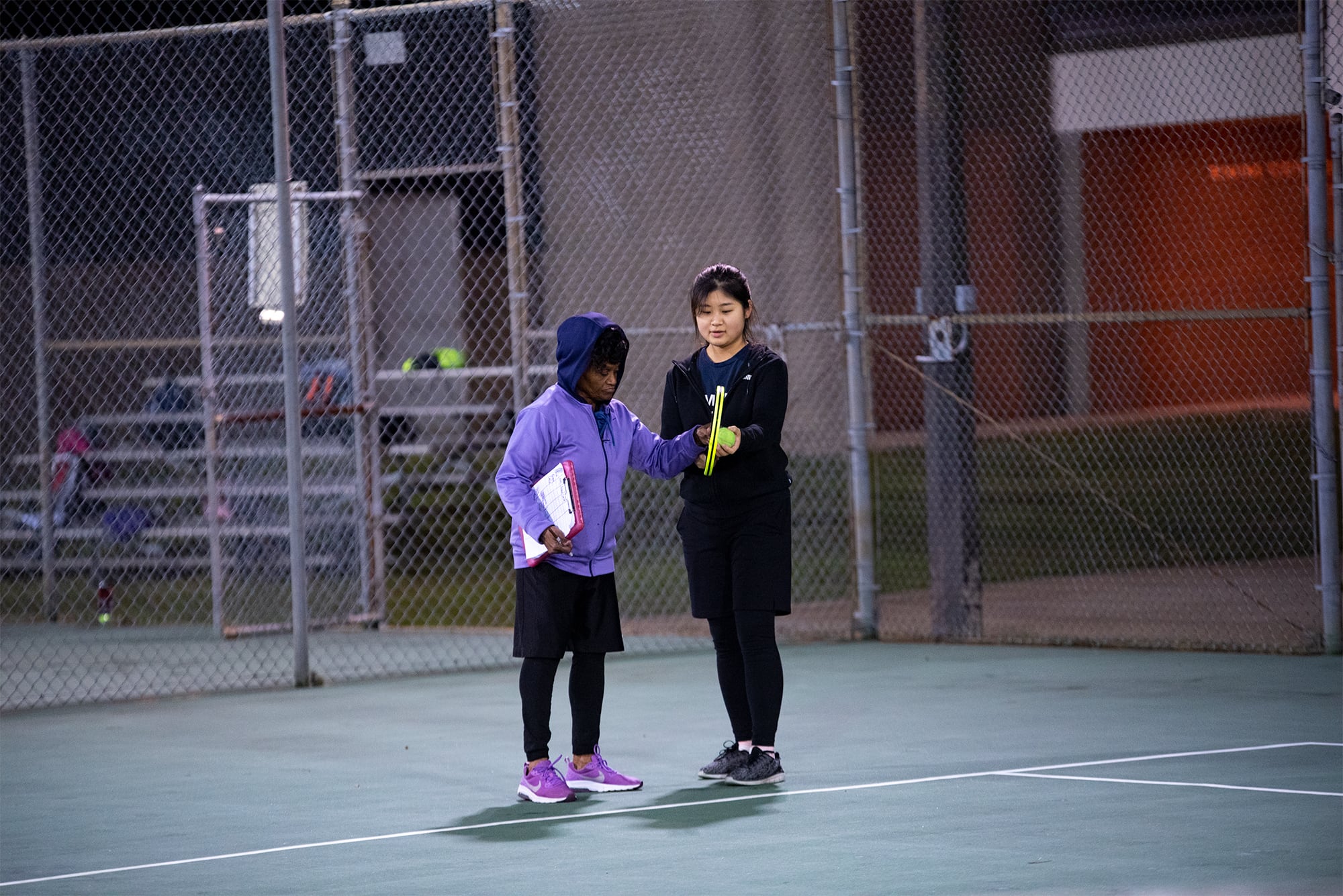 A female teacher instructing a female student in tennis class.