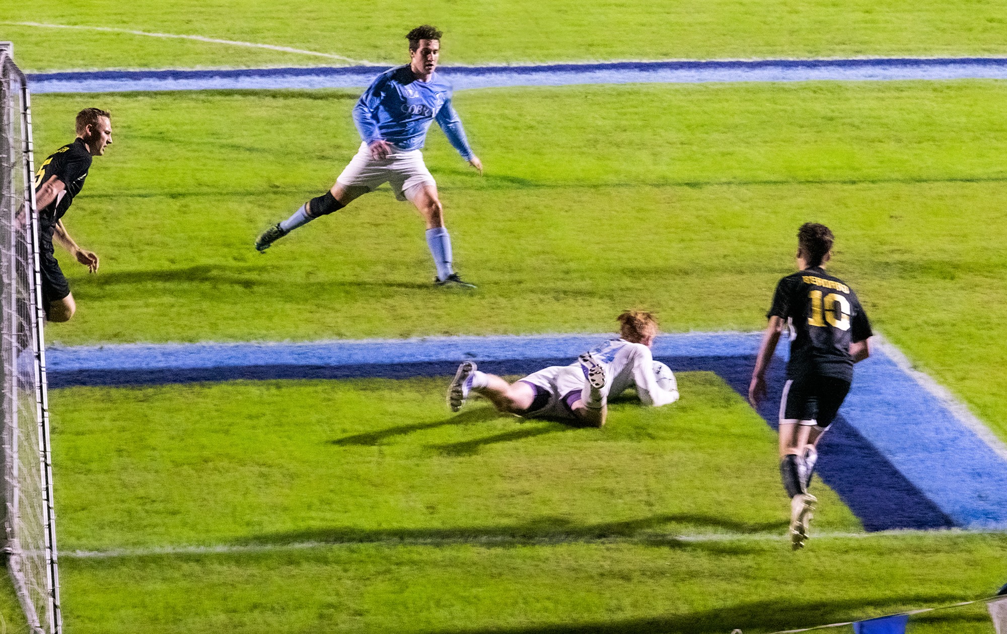 Cobras collegian's goalie holding soccer ball on the ground in front of the goal. 