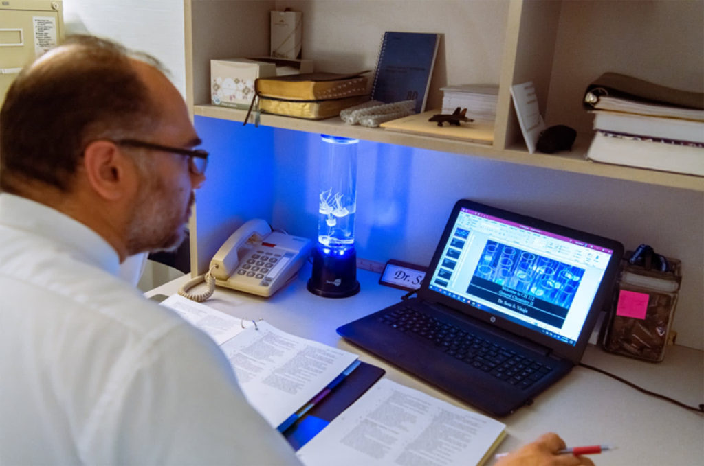 Dr. Sean Vinaja sitting at a desk and looking at a laptop. 