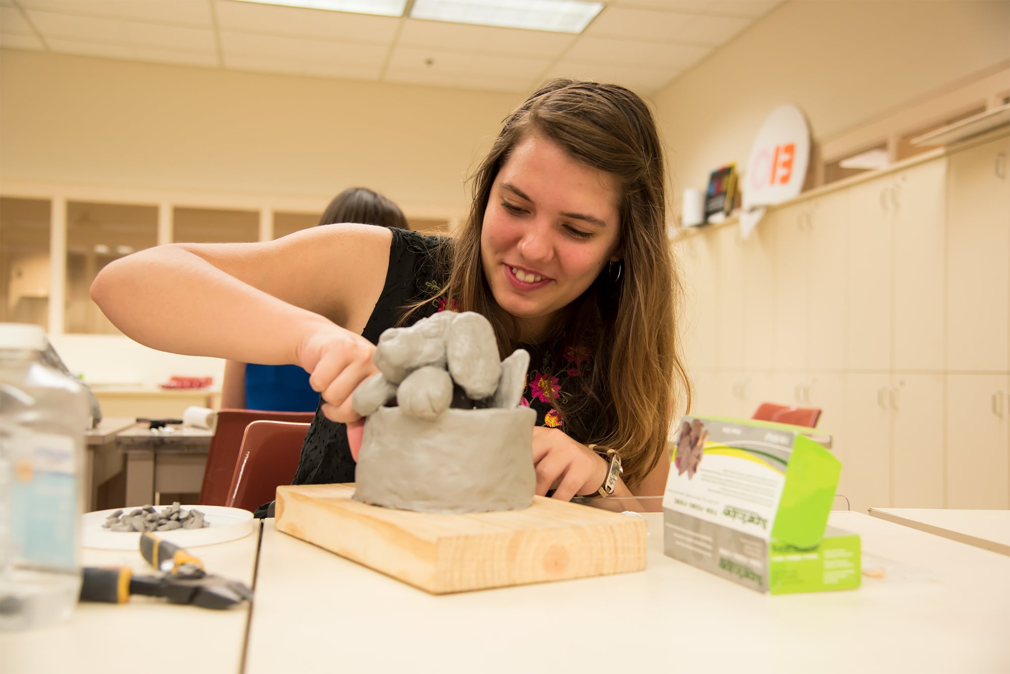 A female Visual Arts students works on a sculpture of a dog in 3D Design Fundamentals