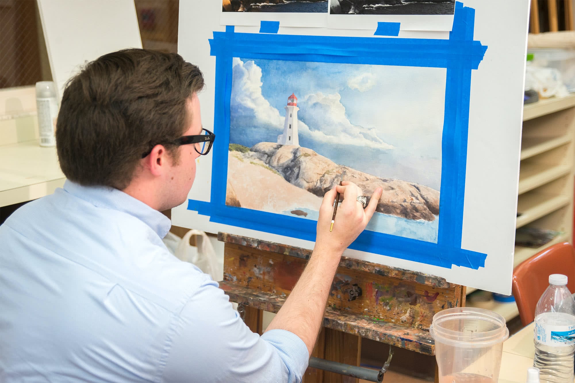 a male Visual Arts student works on a watercolor painting of a lighthouse