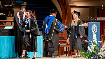 Dr. Shoemaker shaking hands with graduate walking across Crowne Centre stage
