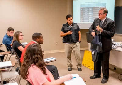 A male professor shows students a bulletproof vest in a criminal justice class