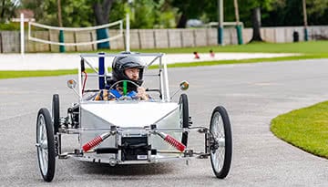 Male student making a turn in a silver electric vehicle during a race.