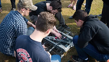 Four male PCC students surrounding their small machine.