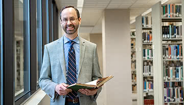 Dr. Rob Achuff standing with a book in the library.