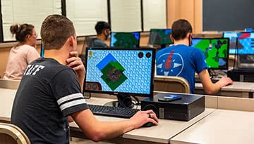 Male student sitting at a computer and playing a video game.