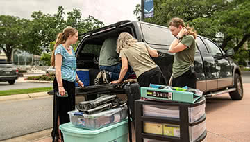 A mom helps her two daughters pack a car full of stuff