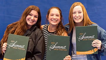 Three female students smiling and holding Summit yearbooks.